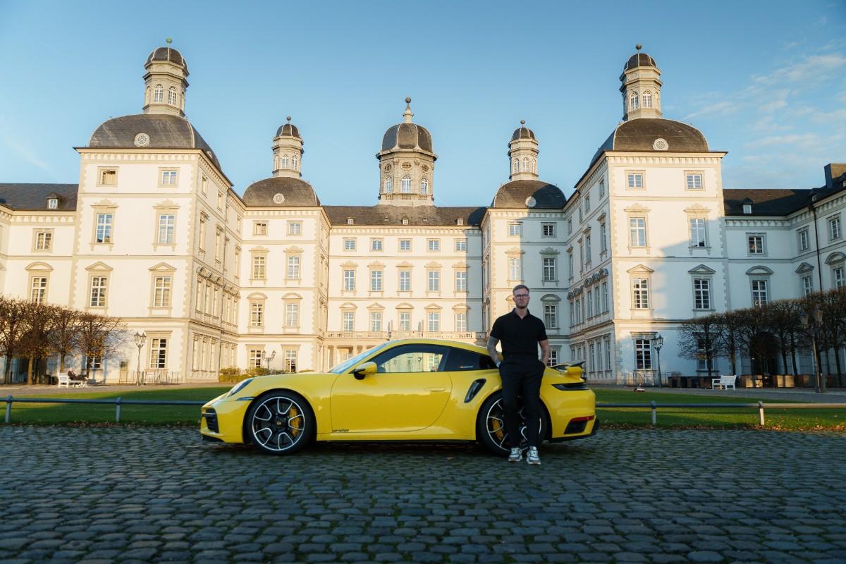 Ein Mann lehnt lässig an einem hochwertigen, gelben Sportwagen vor einem imposanten Schloss. Das Bild verdeutlicht die Bedeutung von Timeboxing für Entscheider: Es symbolisiert den Erfolg und die Freiheit, die durch gezielte Zeitblöcke für wichtige Aufgaben entstehen, um maximale Effizienz und beeindruckende Ergebnisse zu erzielen.