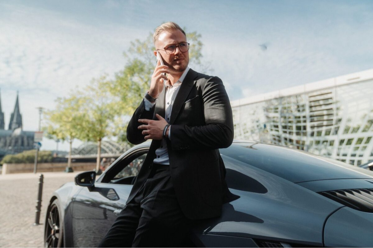 Erfolgreicher Unternehmer telefoniert vor einem Porsche, symbolisch für den Erfolg durch Lean Management Methoden.